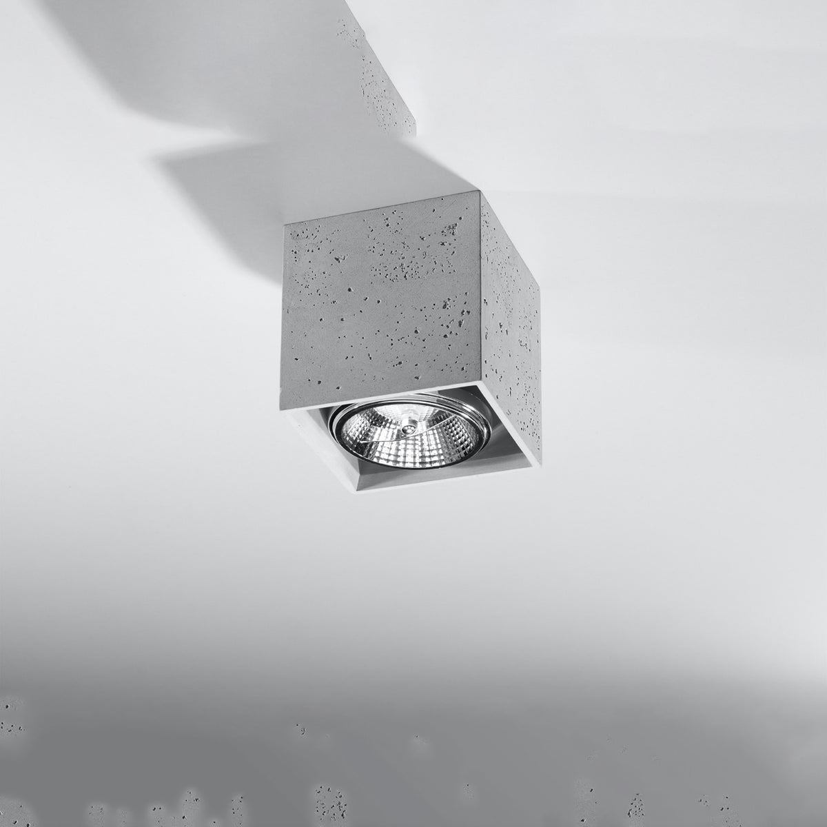 Luminaire carré en béton fixé au plafond blanc, vu de biais