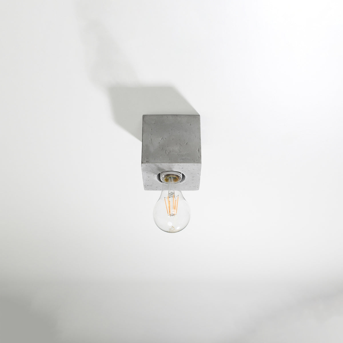 Vue en plongée du luminaire en béton monté au plafond, ombre portée sur fond blanc.