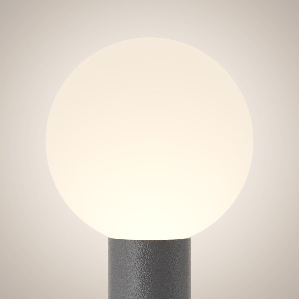 Gros plan du globe blanc lumineux et du sommet du fût cylindrique gris.