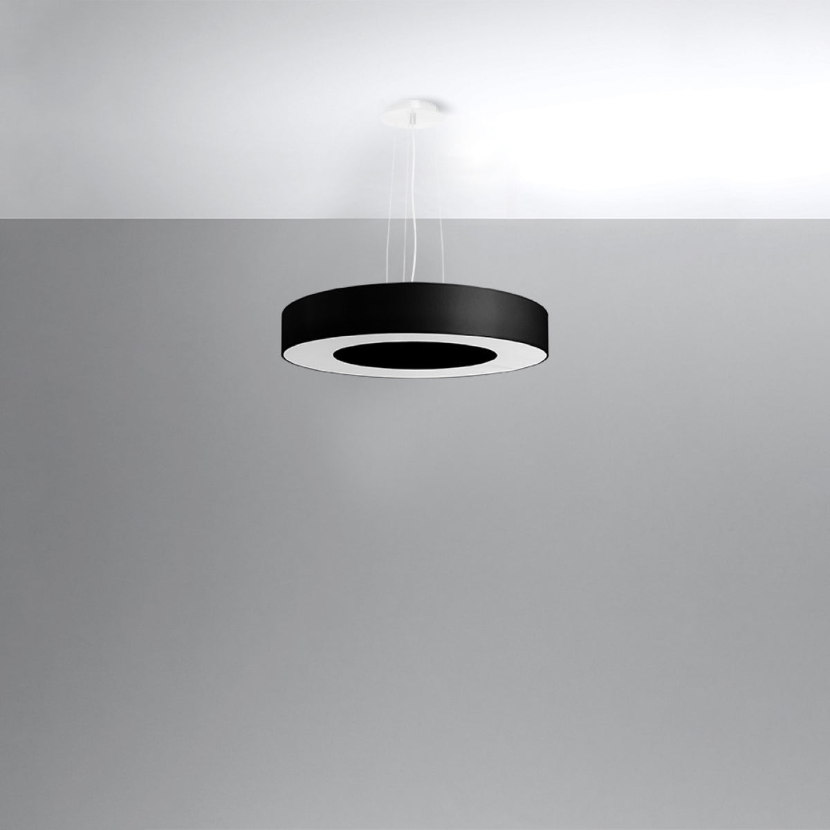 Suspension noire circulaire présentée seule devant un mur gris clair