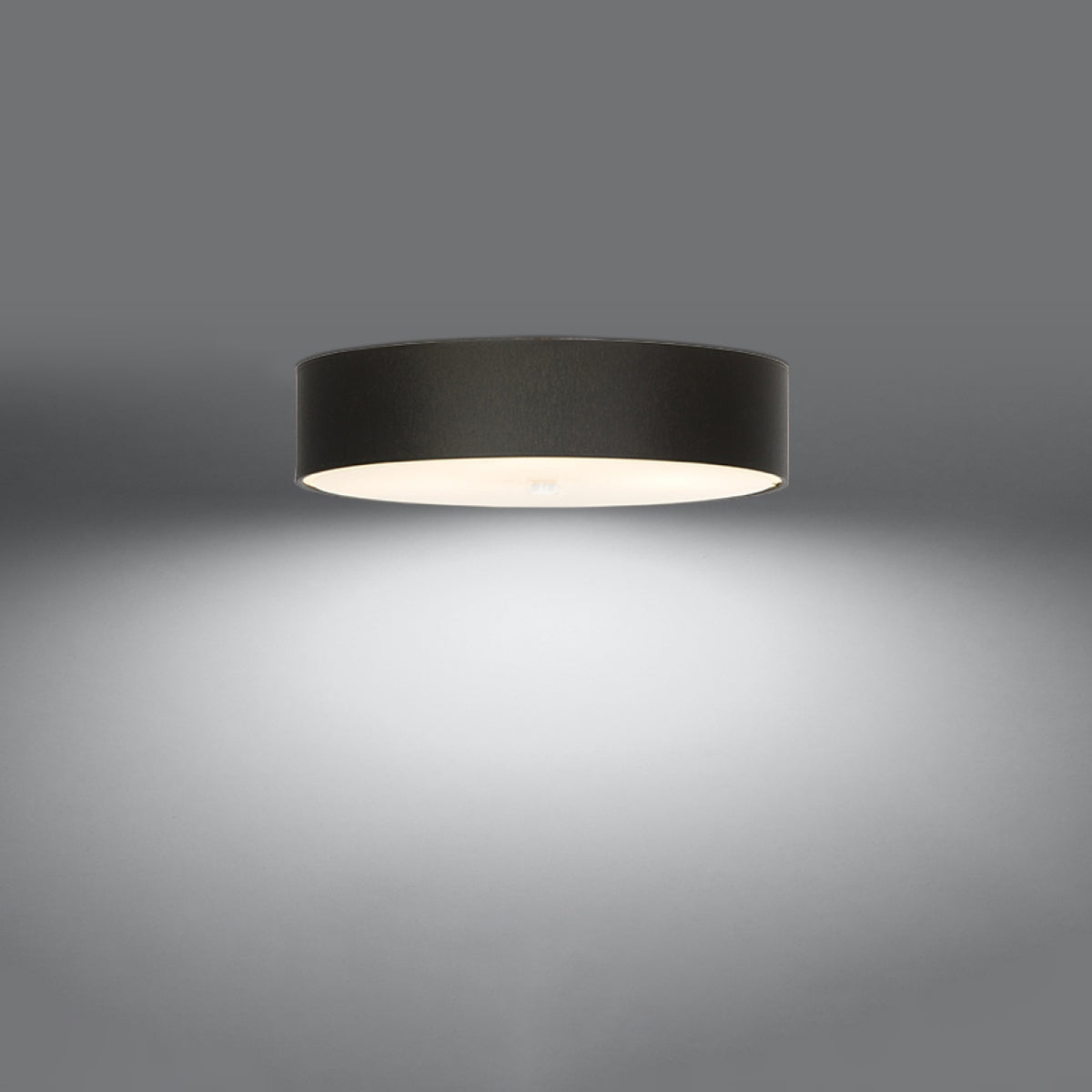 Plafonnier noir allumé au plafond, halo de lumière blanche vers le bas.