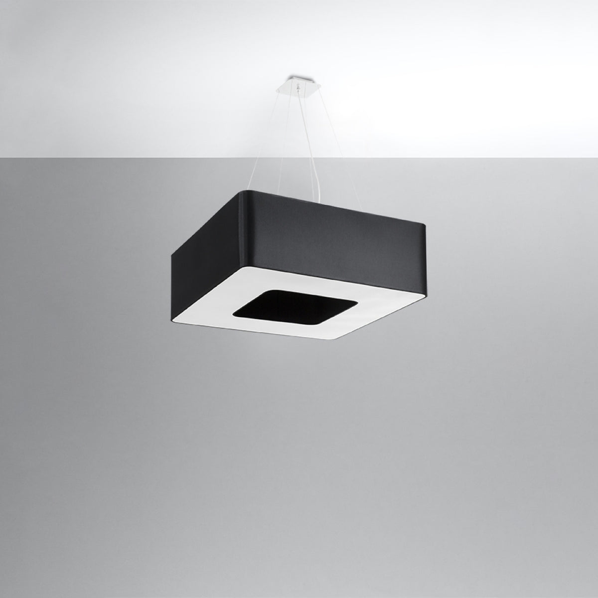 Vue en situation du luminaire suspendu au plafond, câbles apparents et abat-jour noir carré.