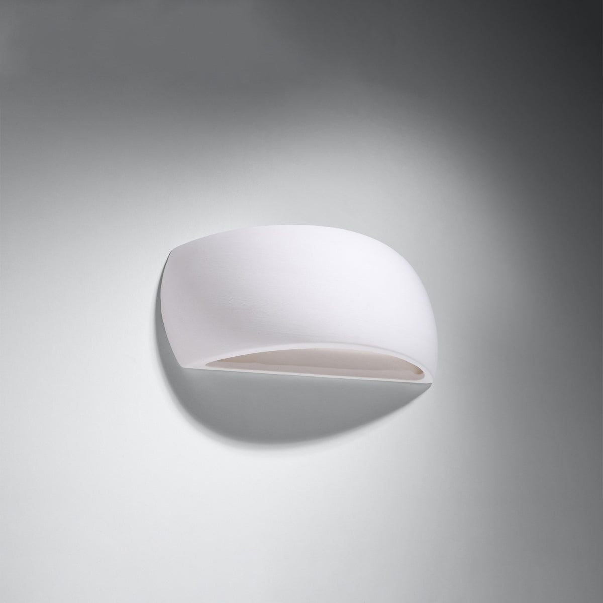 Vue de trois quarts du luminaire non allumé, fixé sur un mur gris clair.