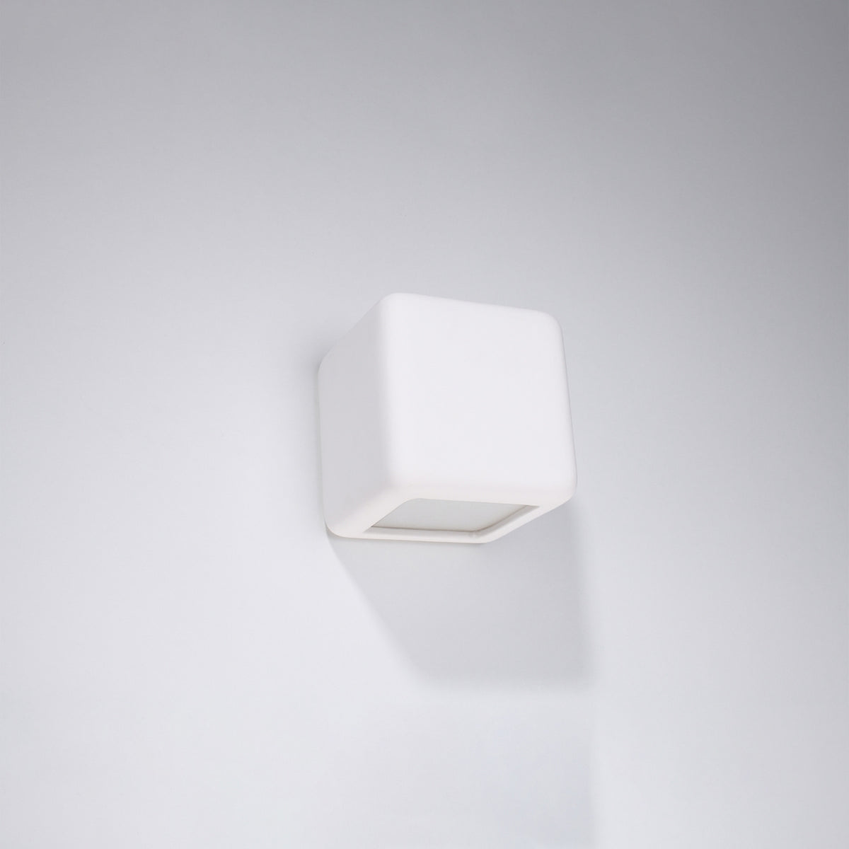 Applique cube blanche fixée sur un mur blanc, vue de face en légère plongée
