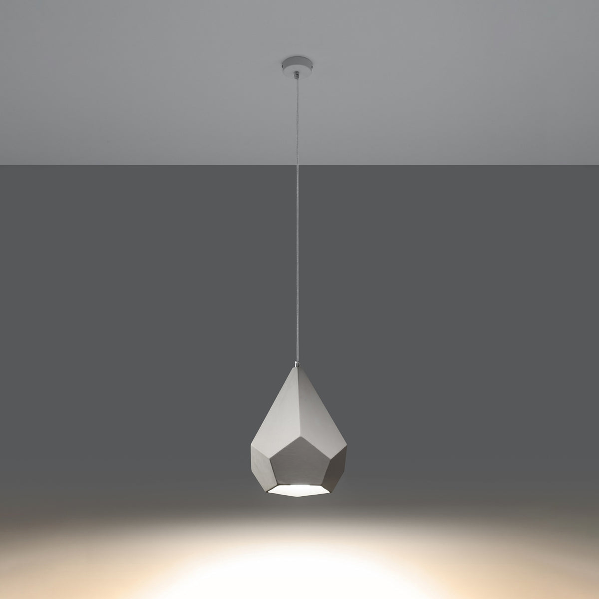 Même suspension céramique blanche allumée, diffusant une lumière chaude vers le sol sombre.