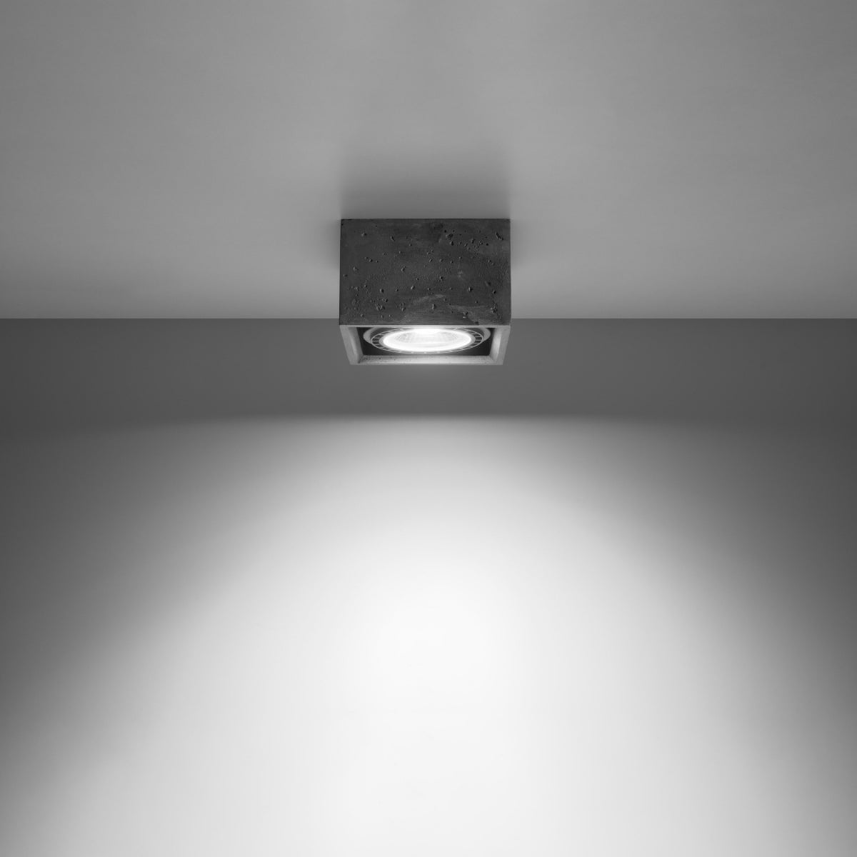 Vue directe sous le plafonnier carré en béton, faisceau lumineux vers le bas.