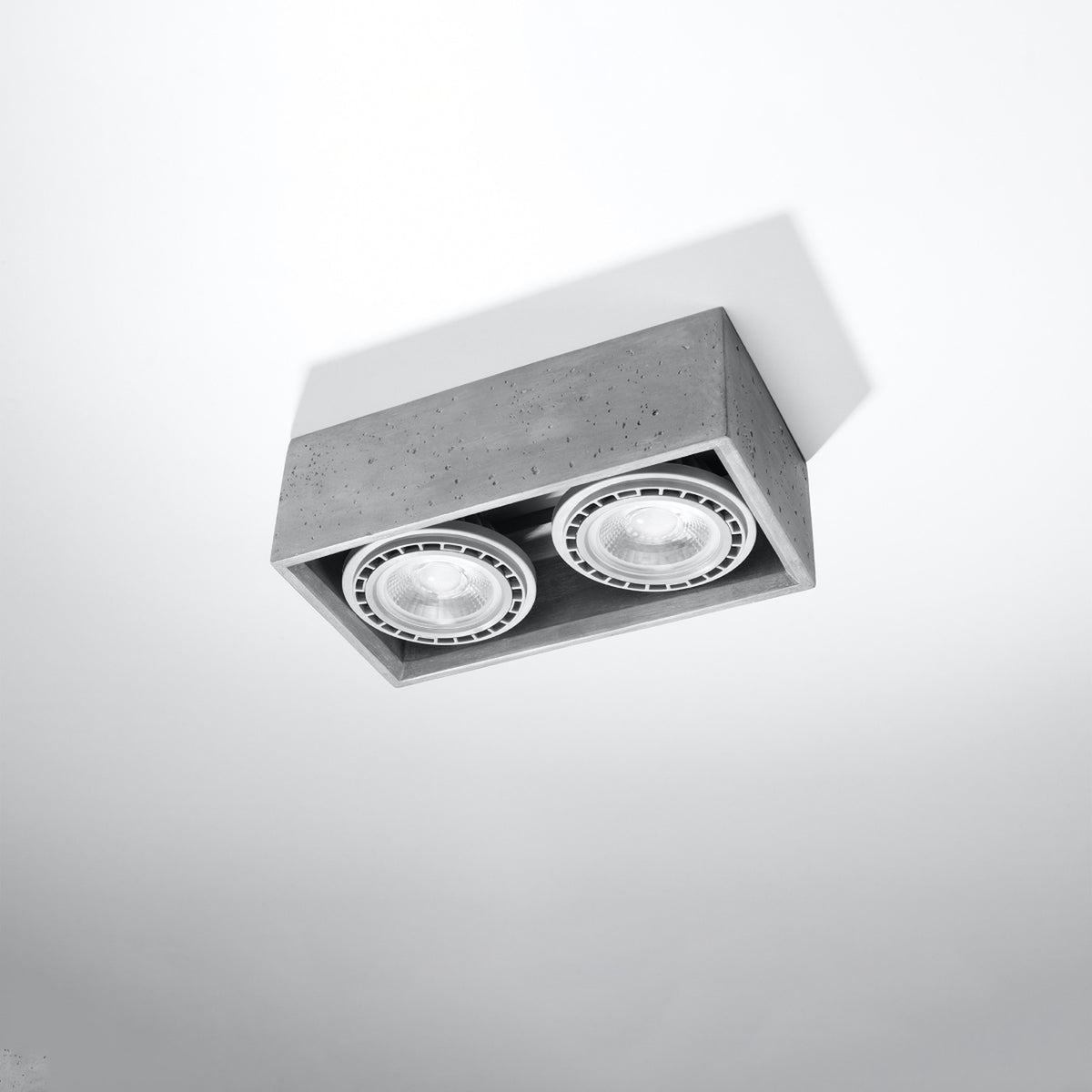 Luminaire en béton installé au plafond blanc, éclairant vers le bas, vue en contre-plongée.