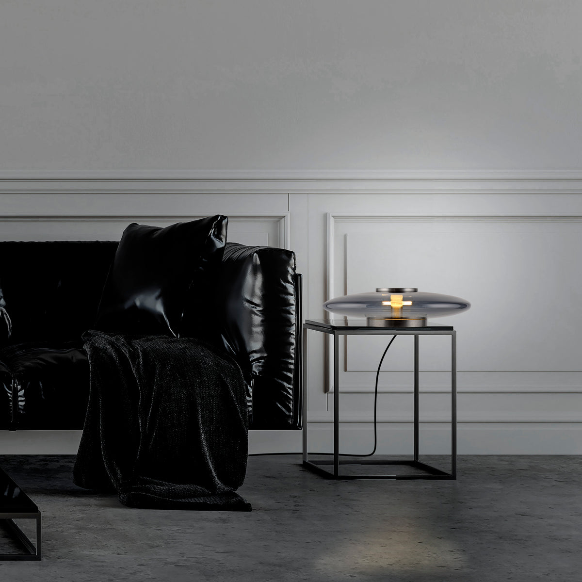 Mise en ambiance sur table d'appoint, lampe posée près d'un canapé noir.