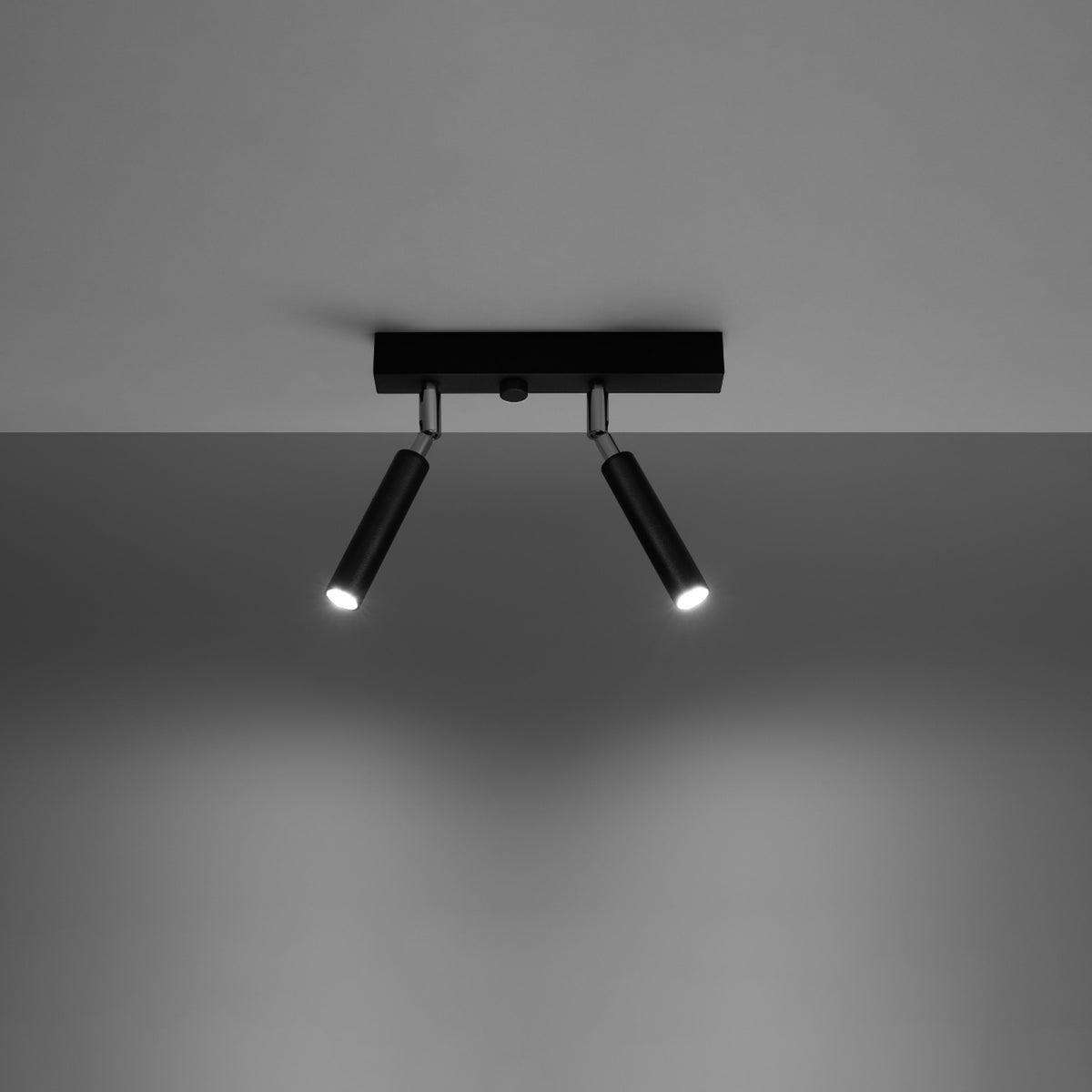 Plafonnier noir allumé, fixé au plafond, deux faisceaux lumineux orientables vers le bas.