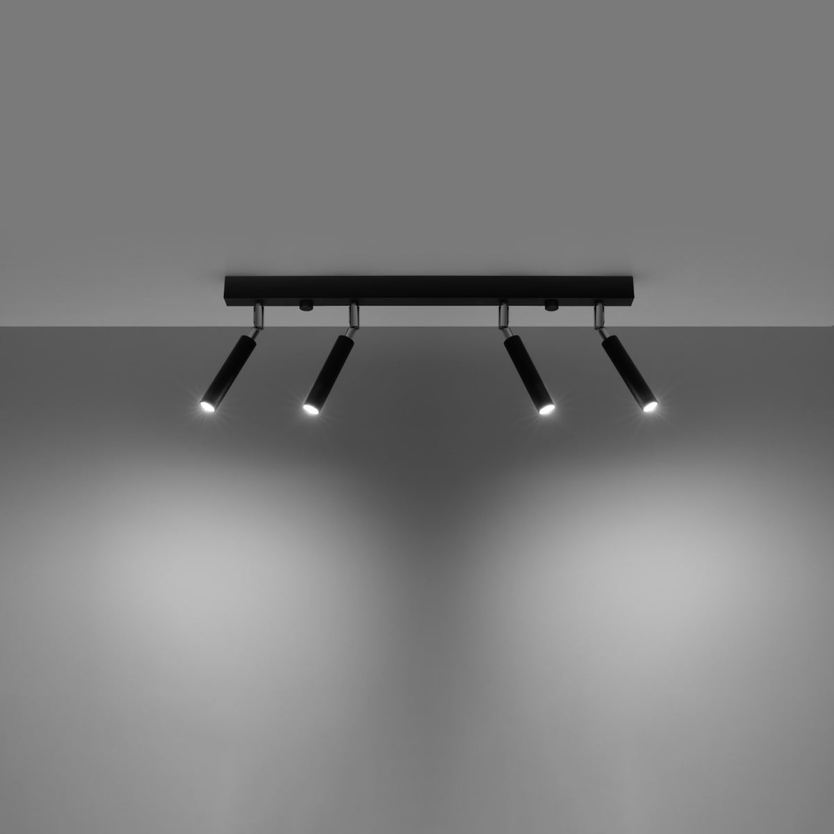Plafonnier allumé éclairant un mur gris avec quatre faisceaux lumineux orientables