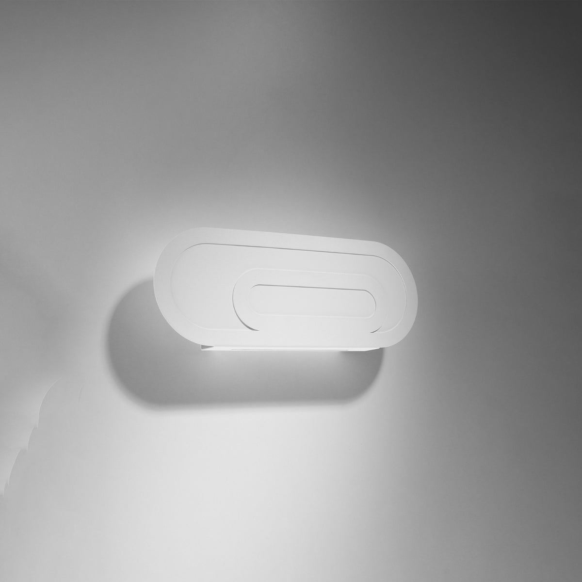 Applique blanche allumée sur mur gris, halo lumineux diffus vers le bas