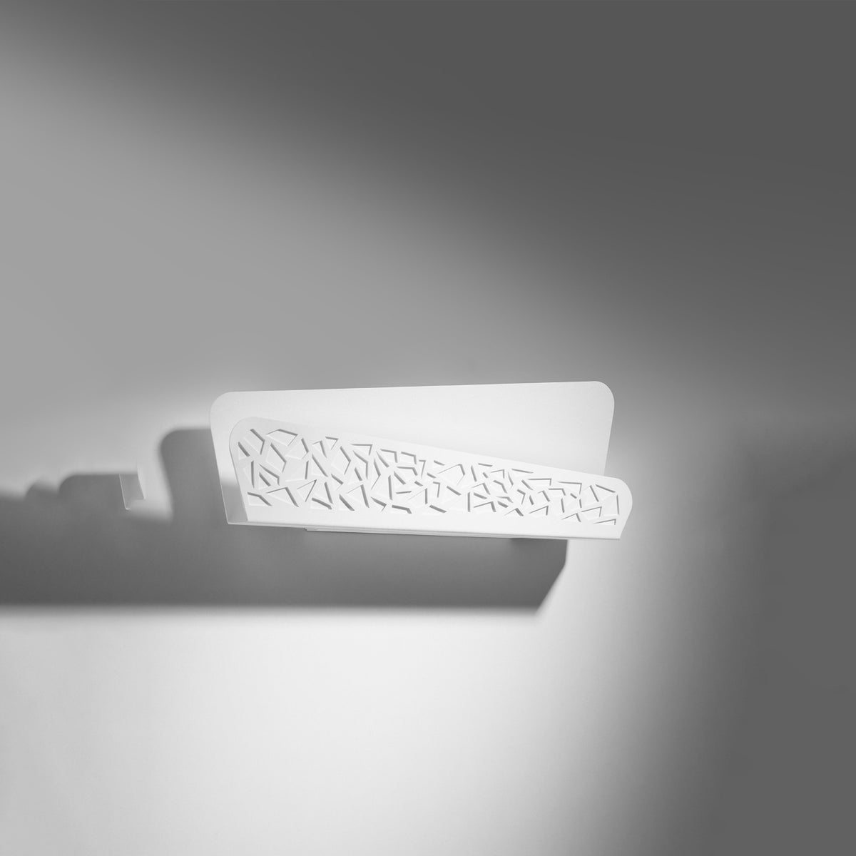 Vue de trois quarts de l'applique fixée au mur, ombre portée sur fond gris.
