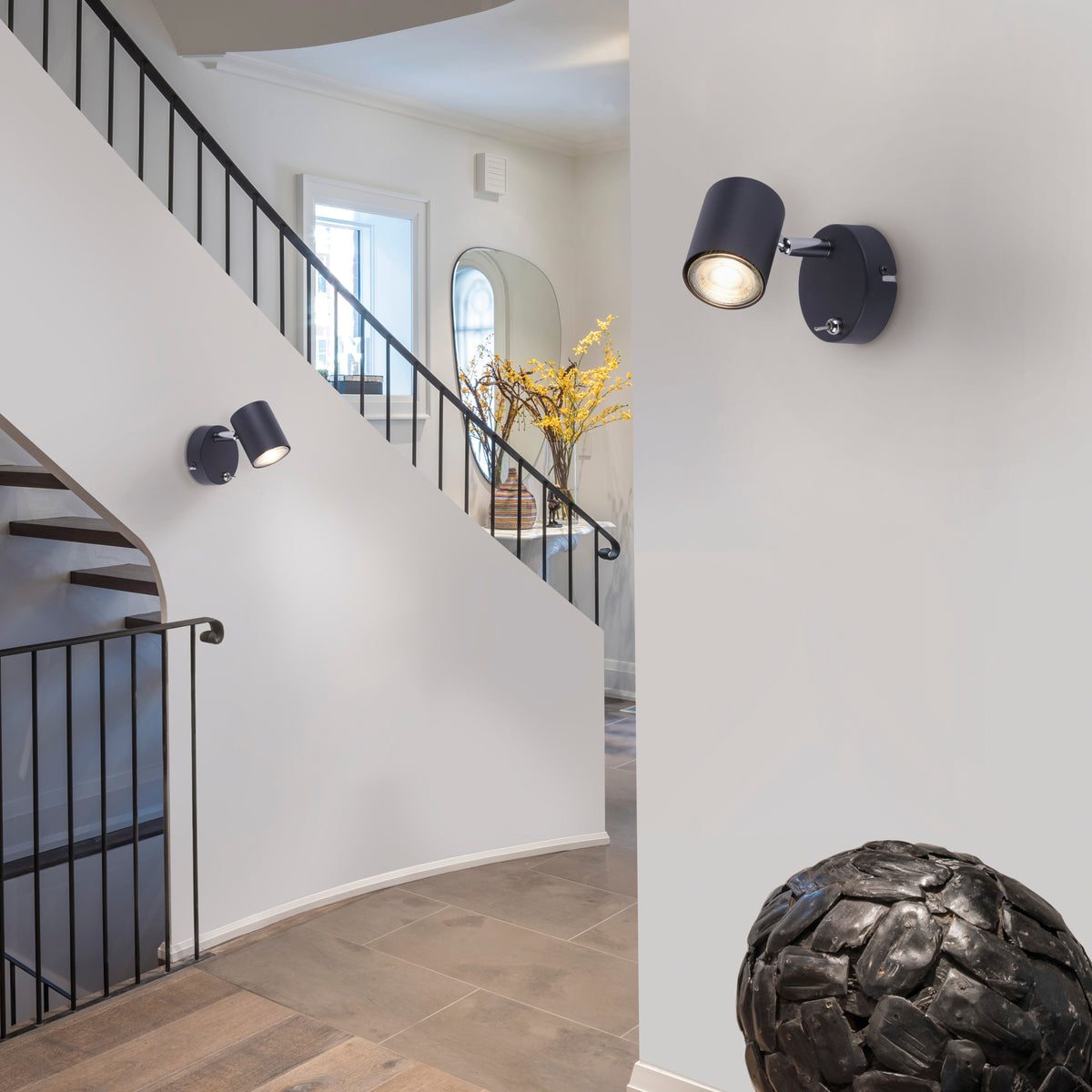 Mise en ambiance dans un escalier blanc, applique murale noire allumée fixée au mur.