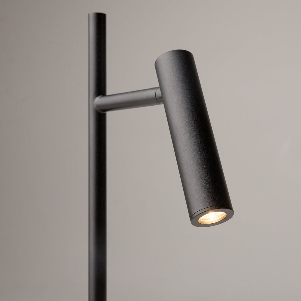 Gros plan sur le projecteur cylindrique noir, lentille LED allumée, finition texturée et rotule.