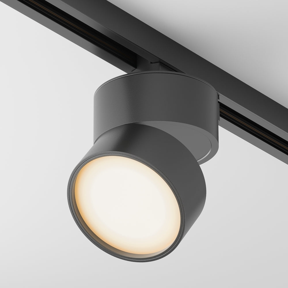 Version noire du spot sur rail, allumée avec une lumière chaude.