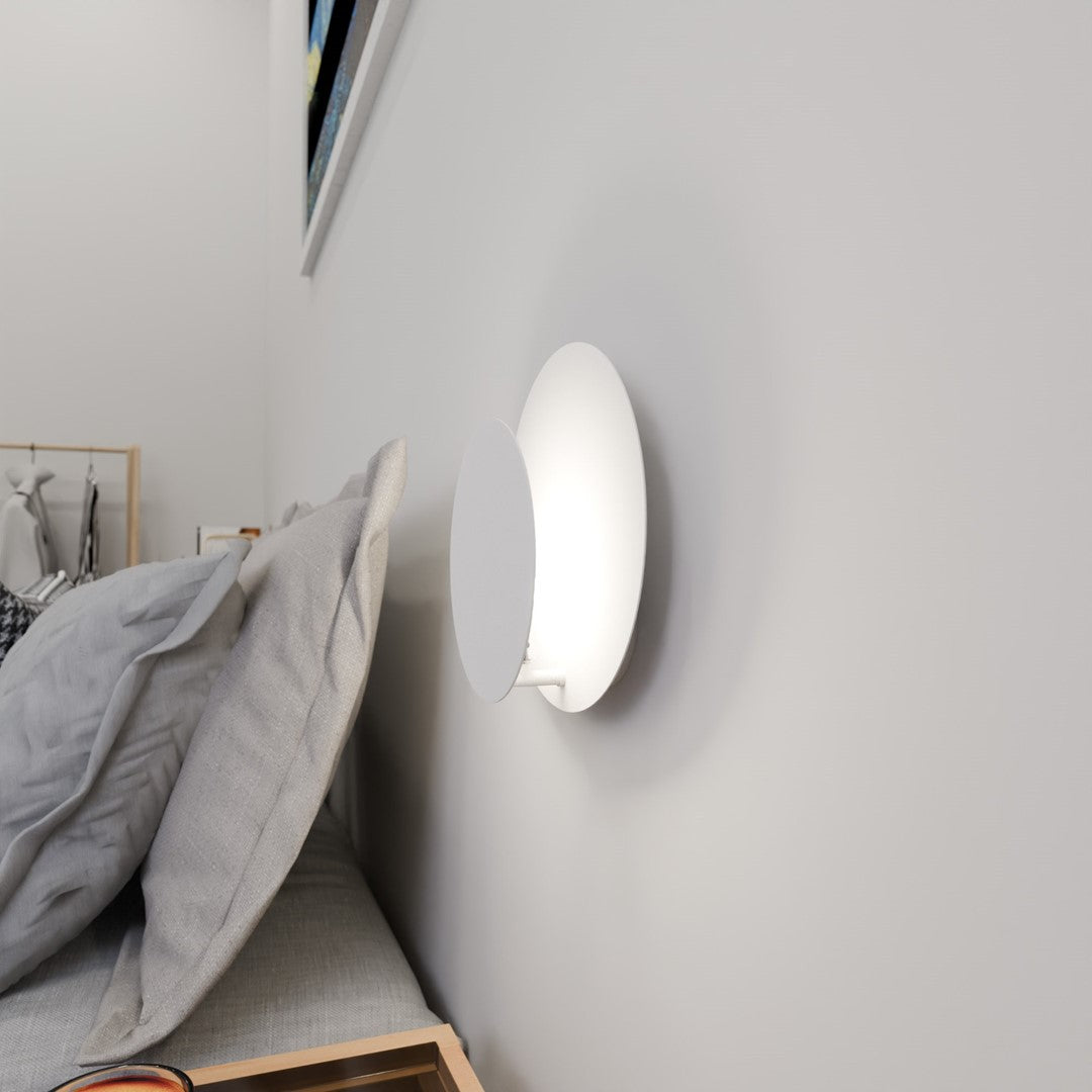 Applique murale allumée fixée au mur près d'un lit, vue de profil avec coussins gris.