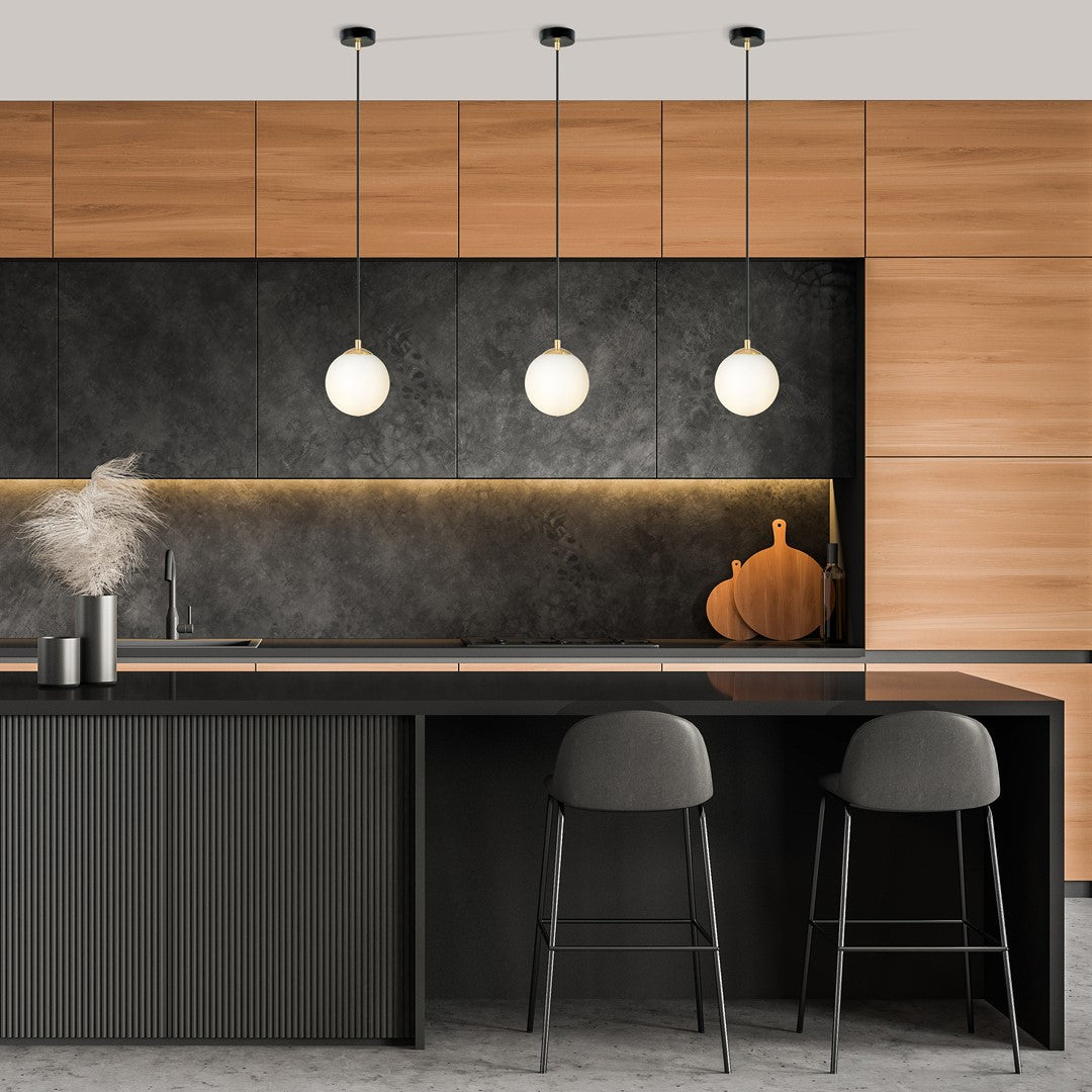 Cuisine sombre avec trois globes lumineux suspendus devant un plan de travail noir