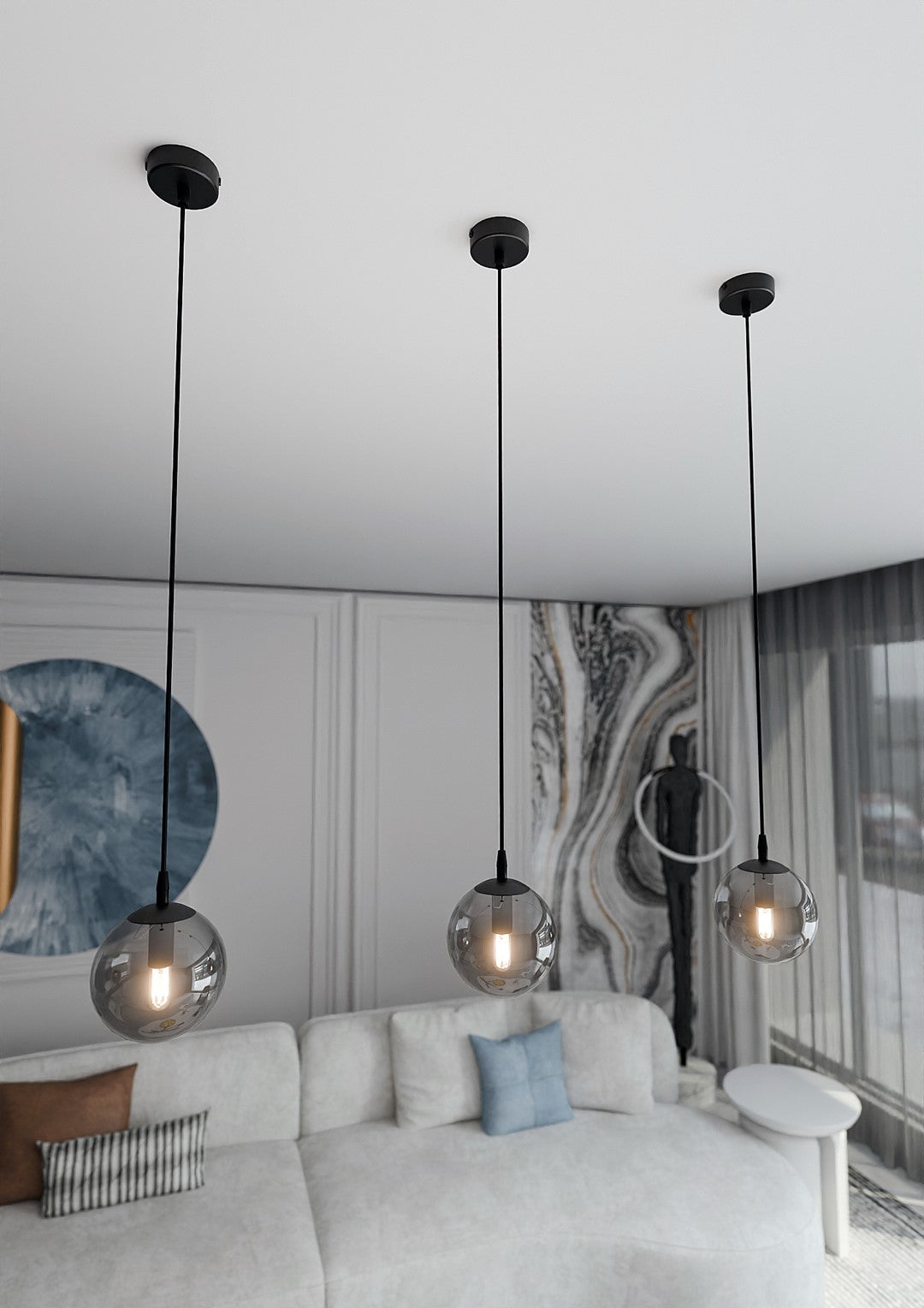 Contre-plongée sur trois globes suspendus éclairés, plafond blanc et canapé clair