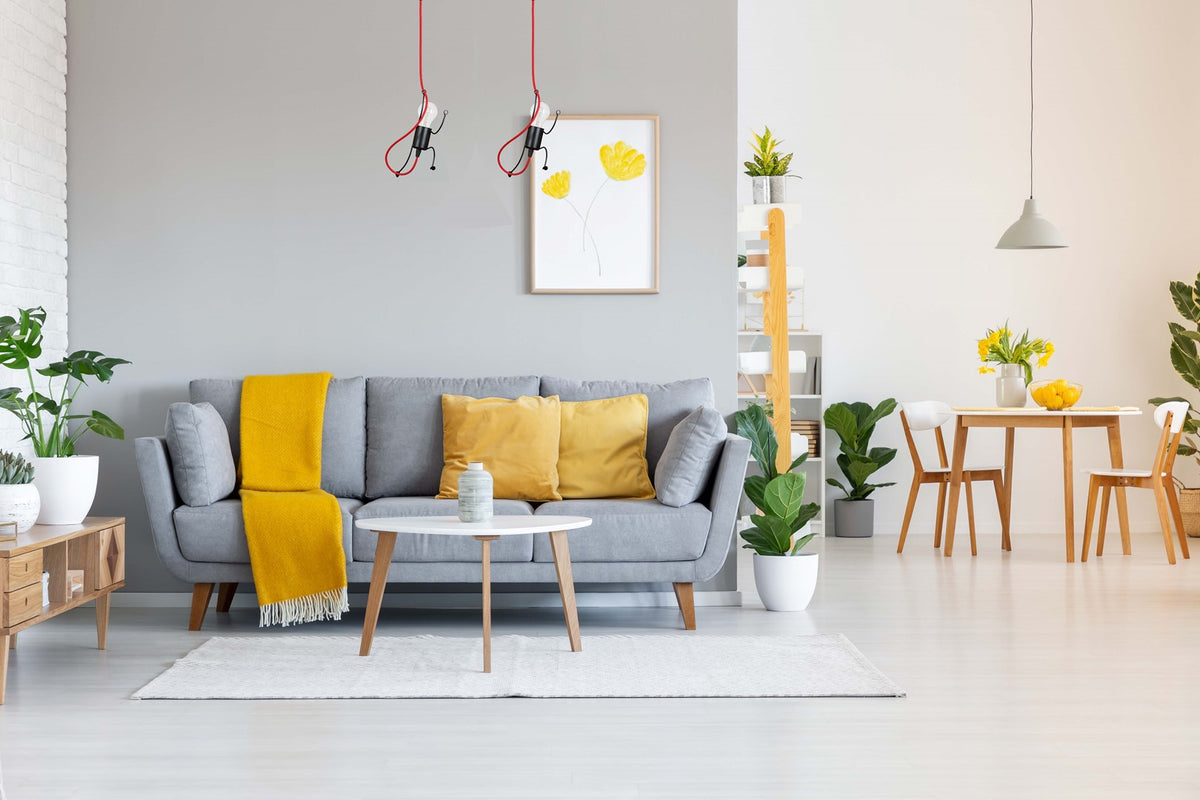 Pièce à vivre lumineuse avec canapé gris, coussins jaunes et suspensions rouges au plafond.