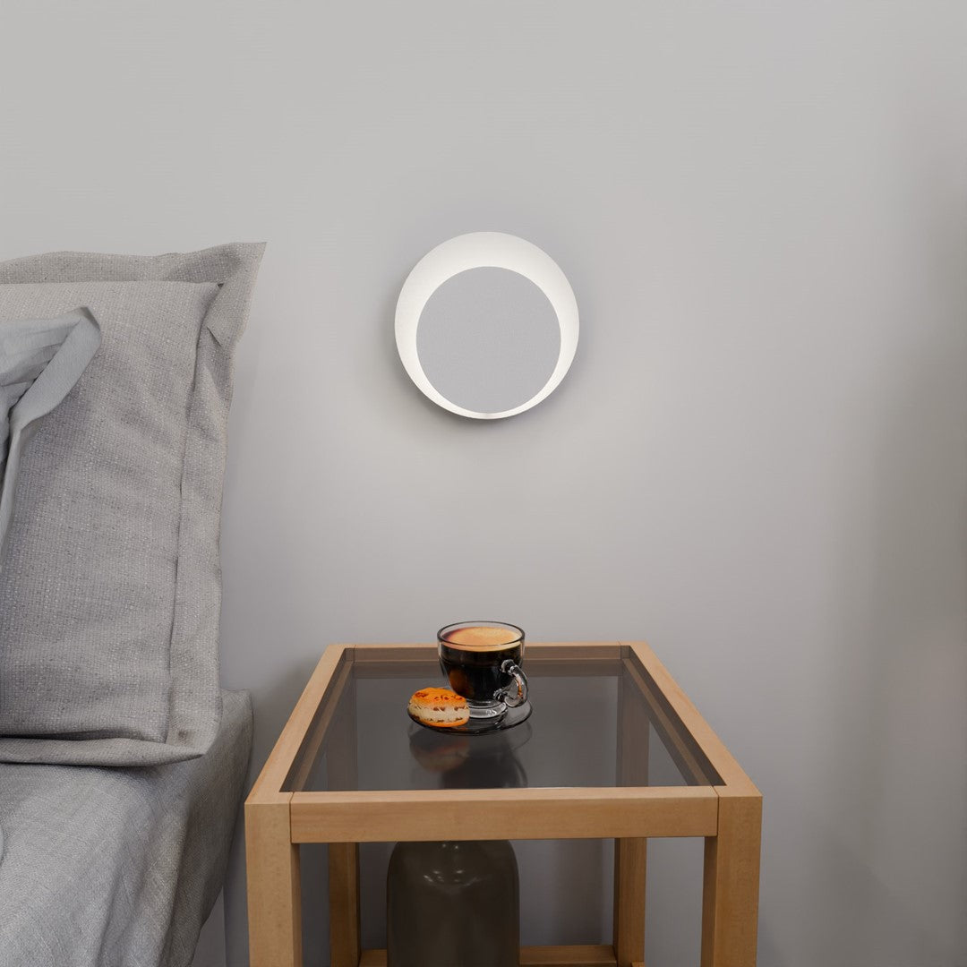 Vue de face de l'applique murale allumée, halo lumineux rond au-dessus d'une table.