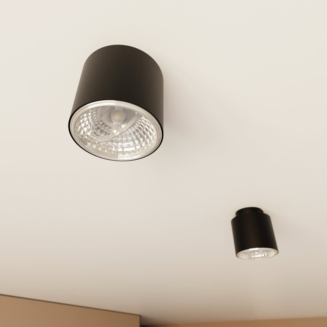 Gros plan sur un plafonnier noir allumé, verre strié et collerette chromée.