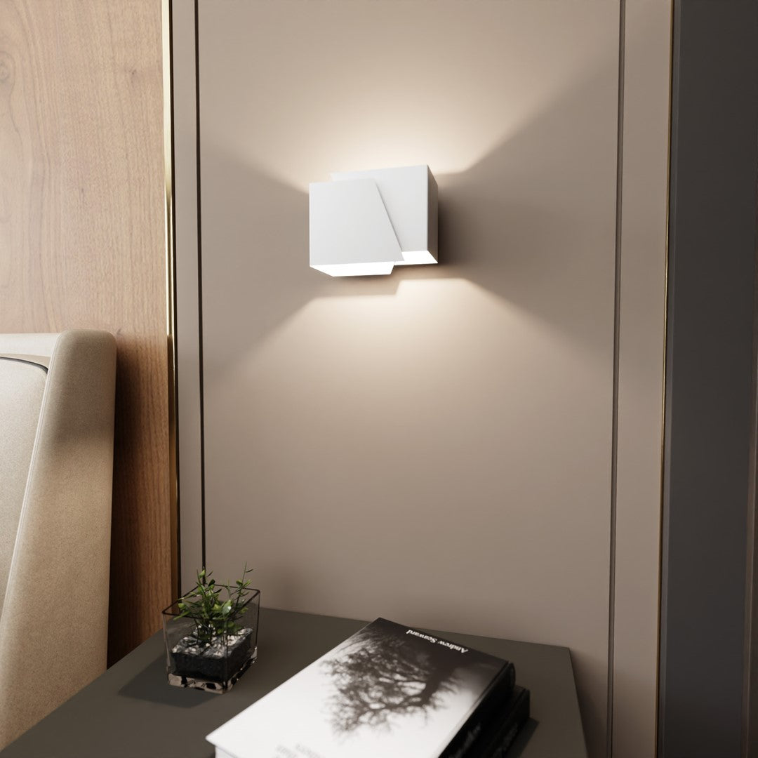 Gros plan sur applique murale blanche allumée, mur beige, livre et plante.
