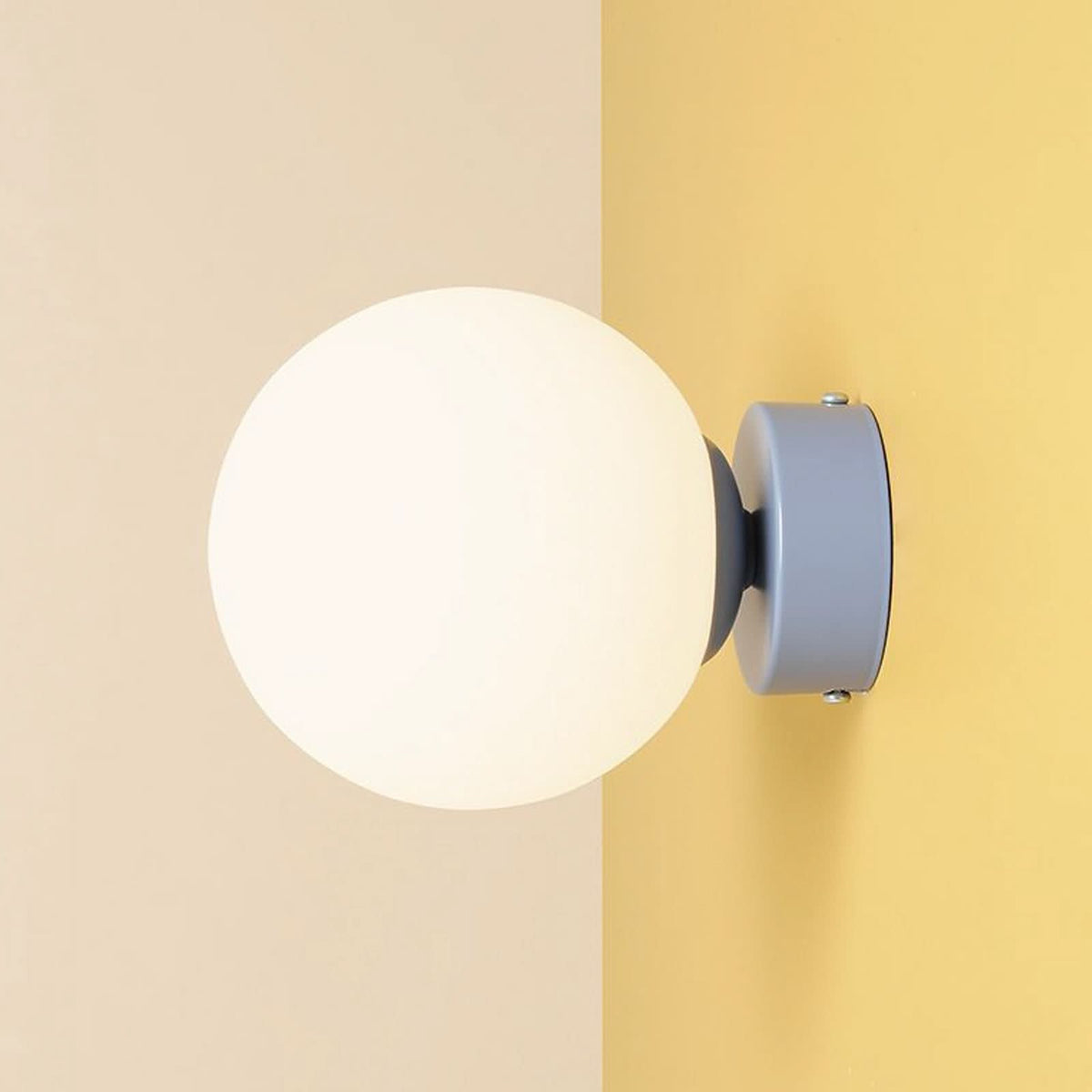 Applique murale au globe blanc lumineux fixé sur un mur jaune pâle.