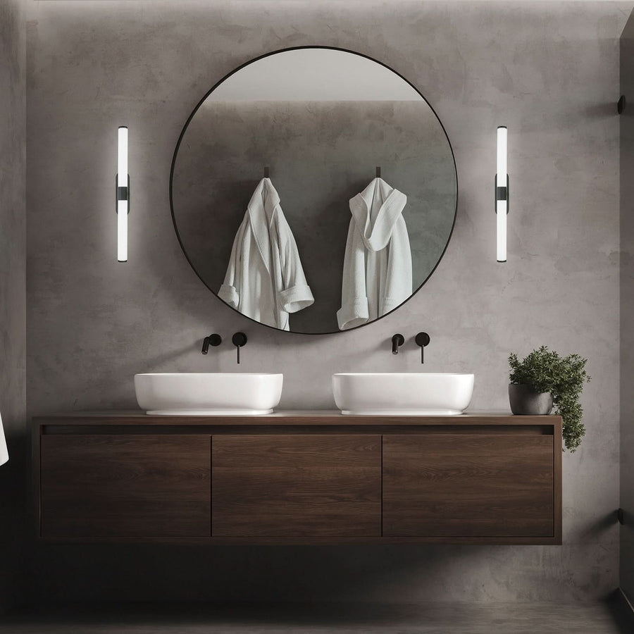 Deux appliques murales verticales encadrent un miroir rond dans une salle de bain.