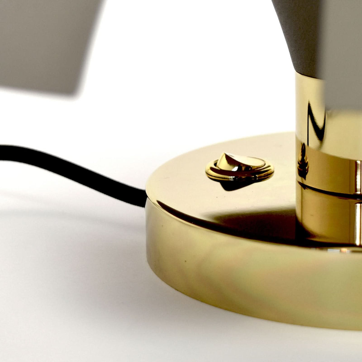 Détail du socle doré, de l'interrupteur et du câble noir sortant.