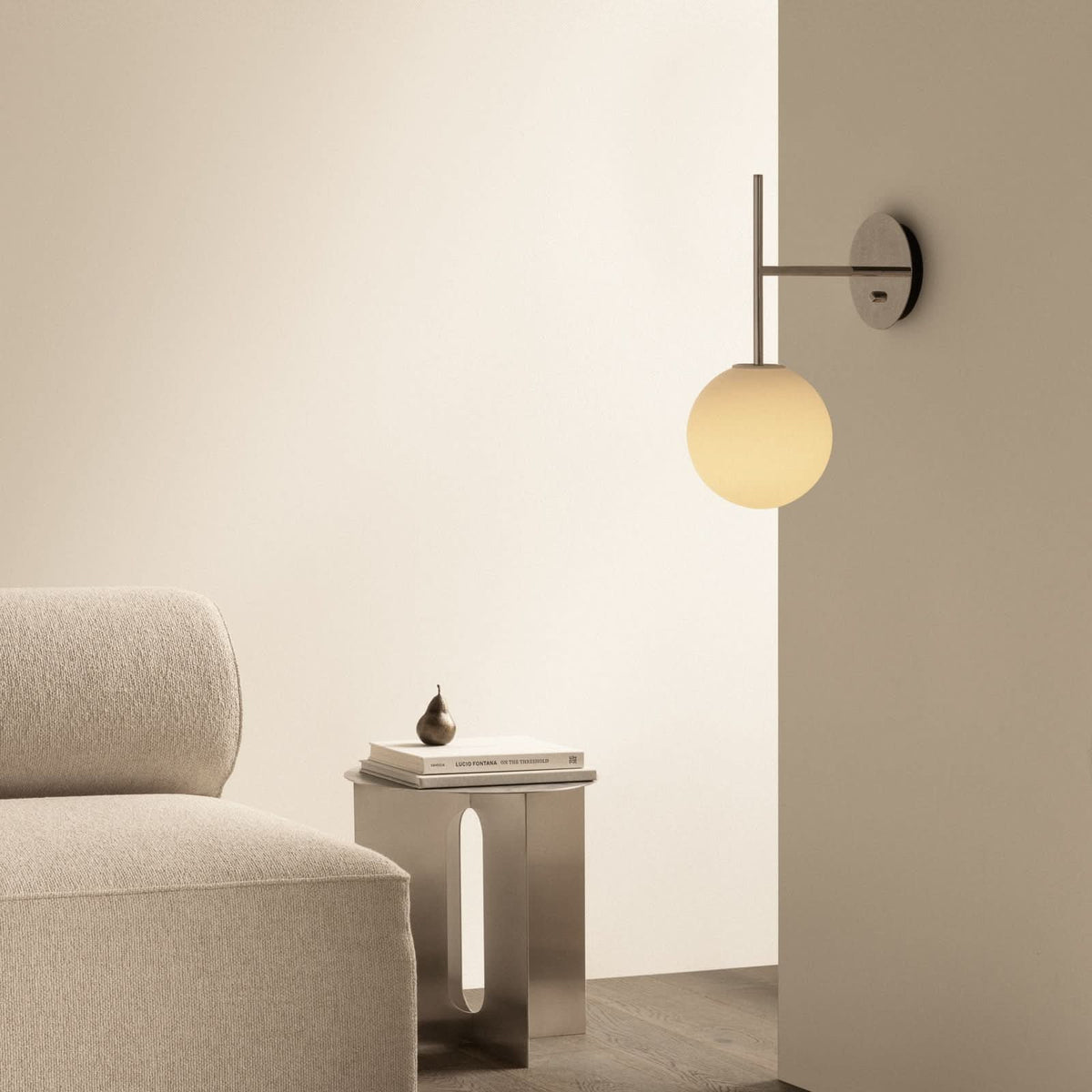 Mise en ambiance : applique murale fixée au mur au-dessus d’un guéridon, fauteuil beige et objets déco.