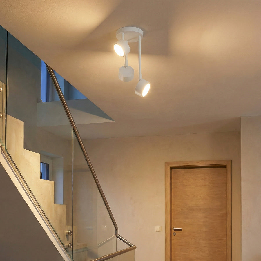 Le luminaire blanc éclaire un escalier avec rampe en verre et porte en bois.