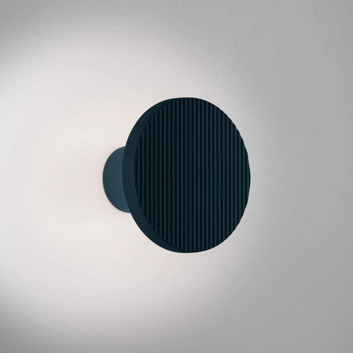 Applique ronde fixée au mur blanc, lumière allumée et halo discret.
