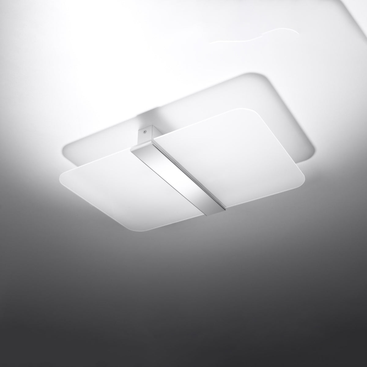 Vue de dessous du luminaire allumé en lumière froide, halo diffus sur le mur