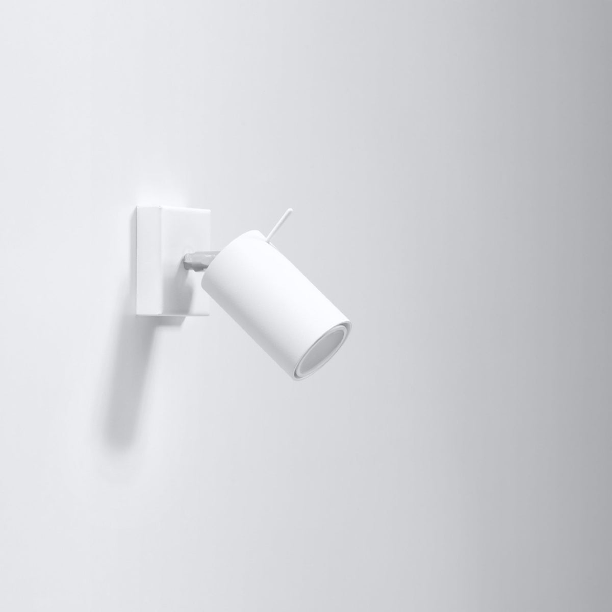 Applique blanche fixée au mur, spot cylindrique orientable vers le bas, interrupteur visible sur la base.