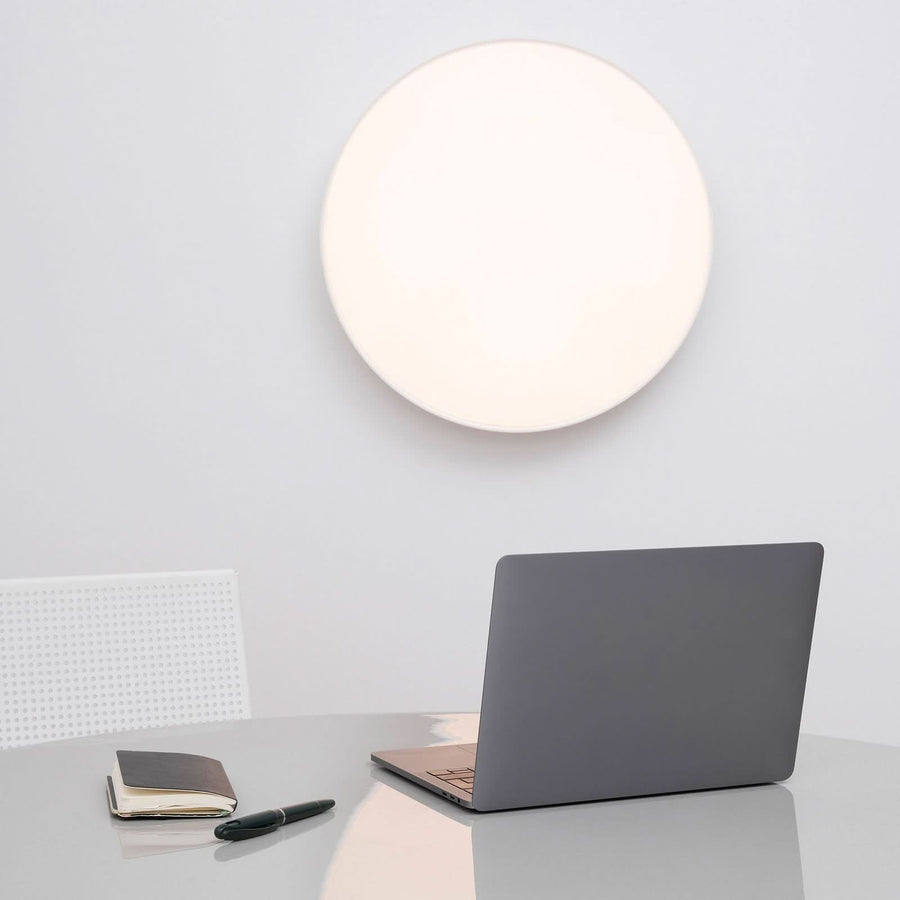 Luminaire mural circulaire allumé, intégré dans un bureau moderne et épuré.