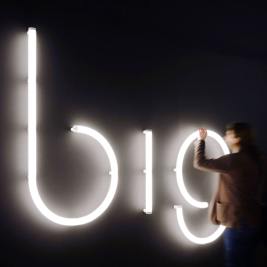 Personne ajustant une grande lettre lumineuse sur un mur noir, vue de côté.