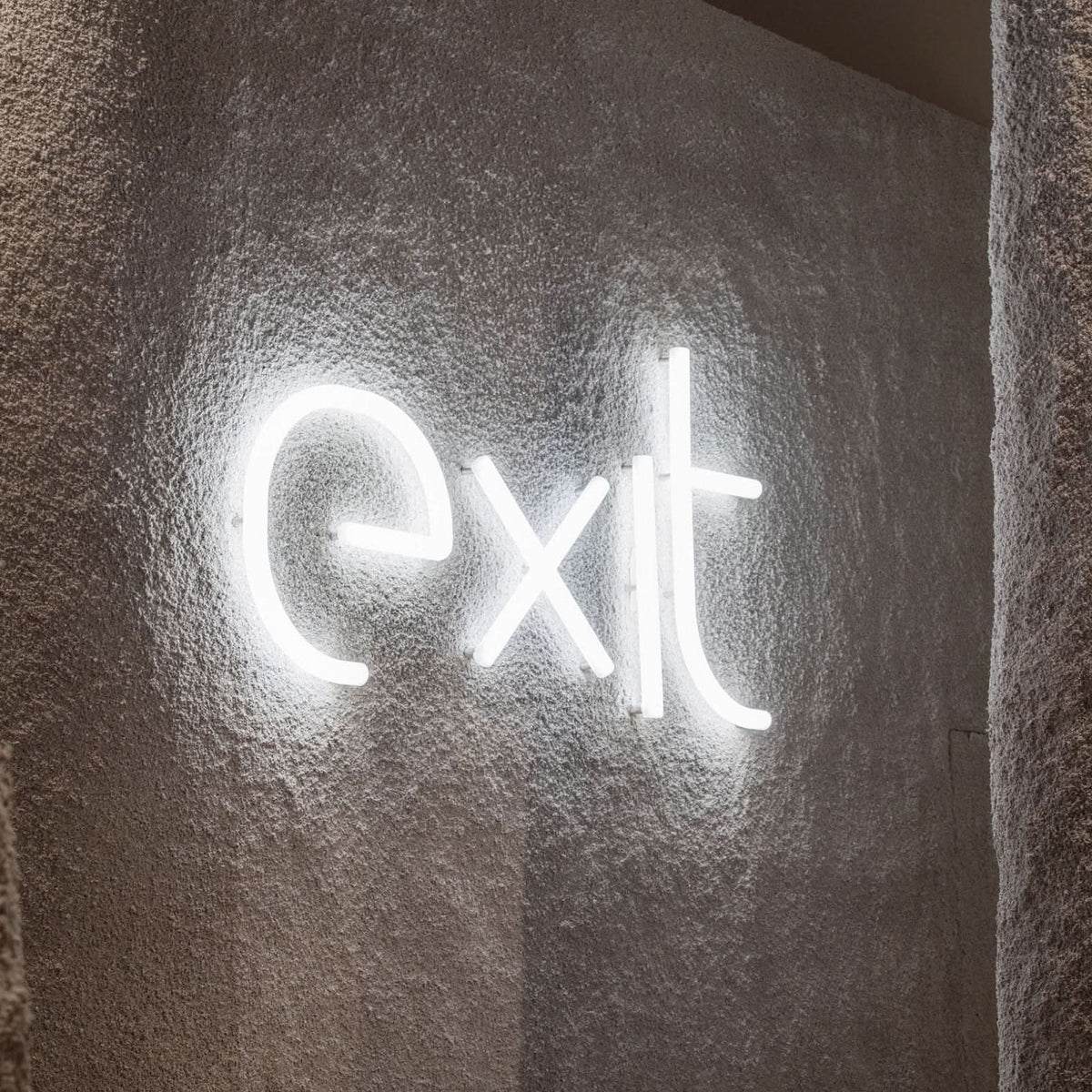 Gros plan du mot exit en lettres LED blanches sur un mur gris rugueux.
