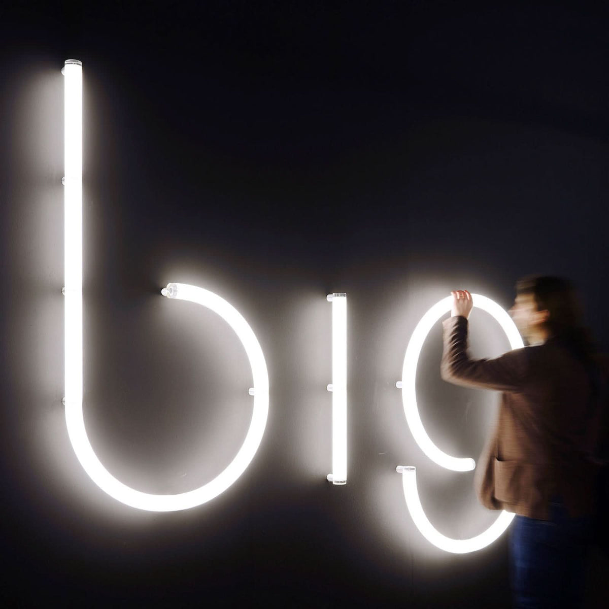 Personne ajustant de grandes lettres lumineuses blanches sur un mur sombre.