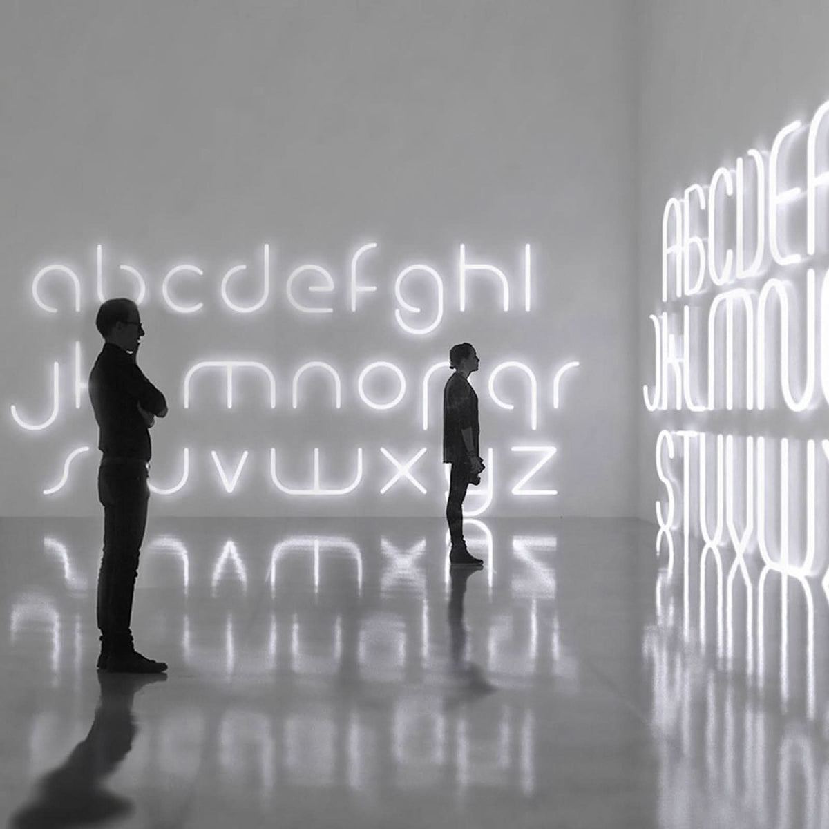 Deux personnes observant une grande installation murale de lettres lumineuses.