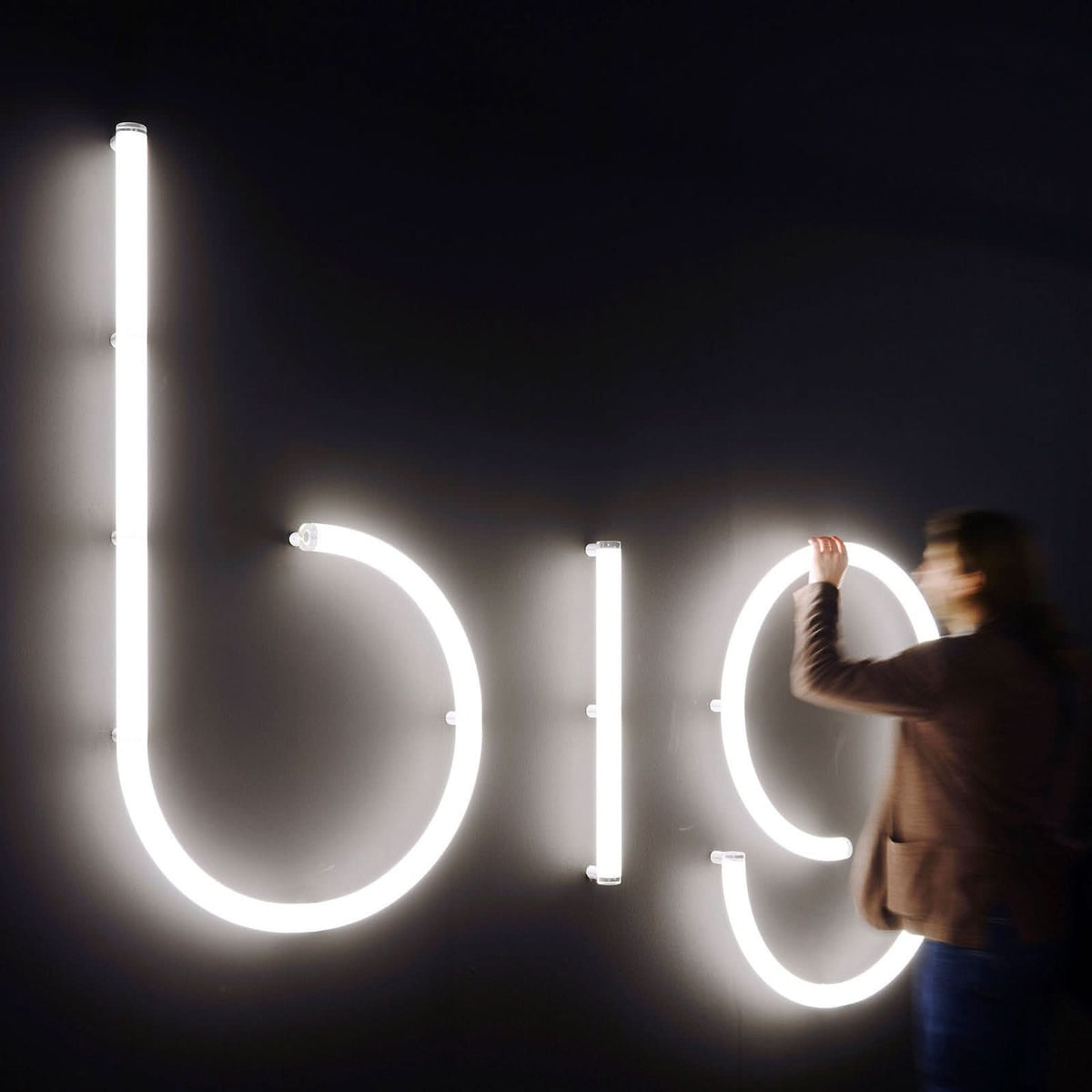 Personne ajustant les lettres lumineuses glob sur un mur sombre.