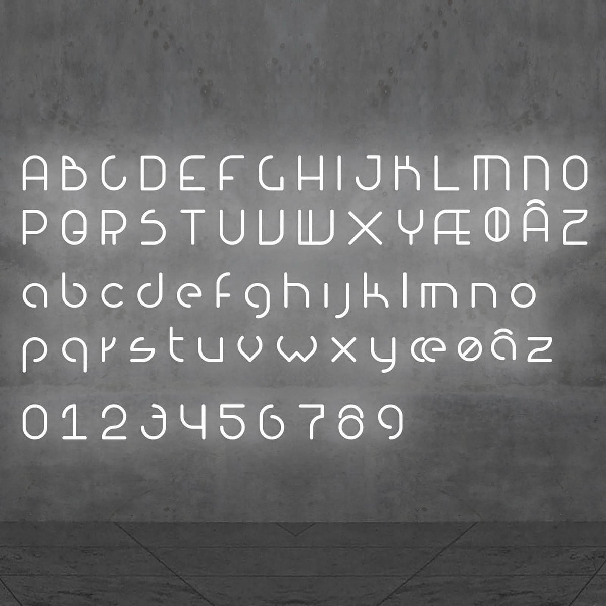 Alphabet complet en lettres blanches lumineuses sur un mur gris.