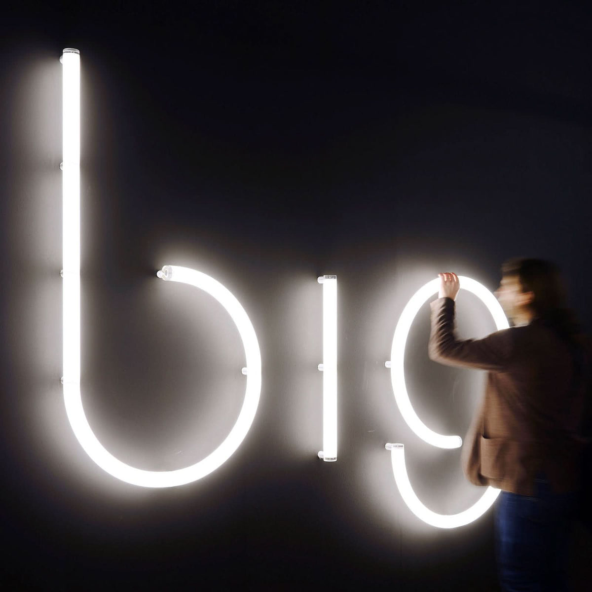 Personne ajustant de grandes lettres lumineuses big sur un mur sombre.