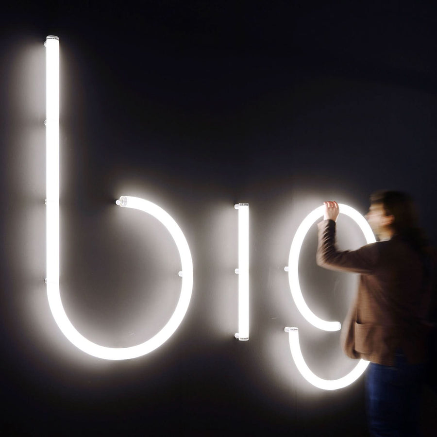 Personne ajustant de grandes lettres lumineuses big sur un mur sombre.
