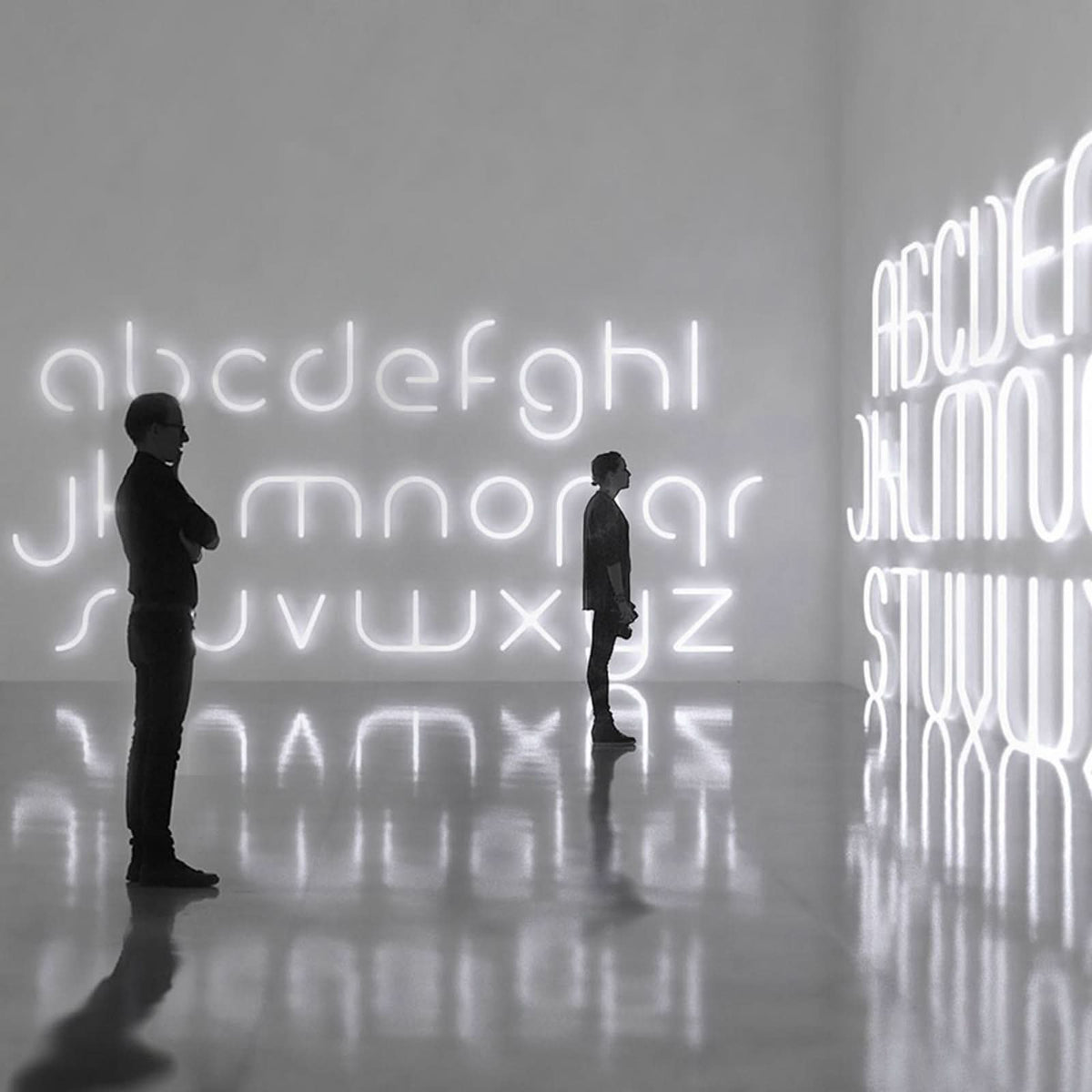 Deux personnes contemplent des lettres lumineuses blanches disposées sur de grands murs.