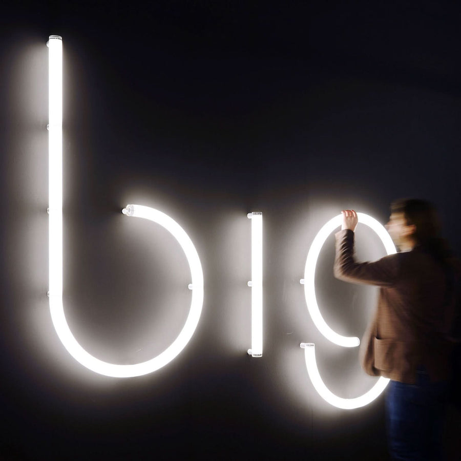 Personne installant une grande enseigne lumineuse à lettres blanches sur un mur sombre