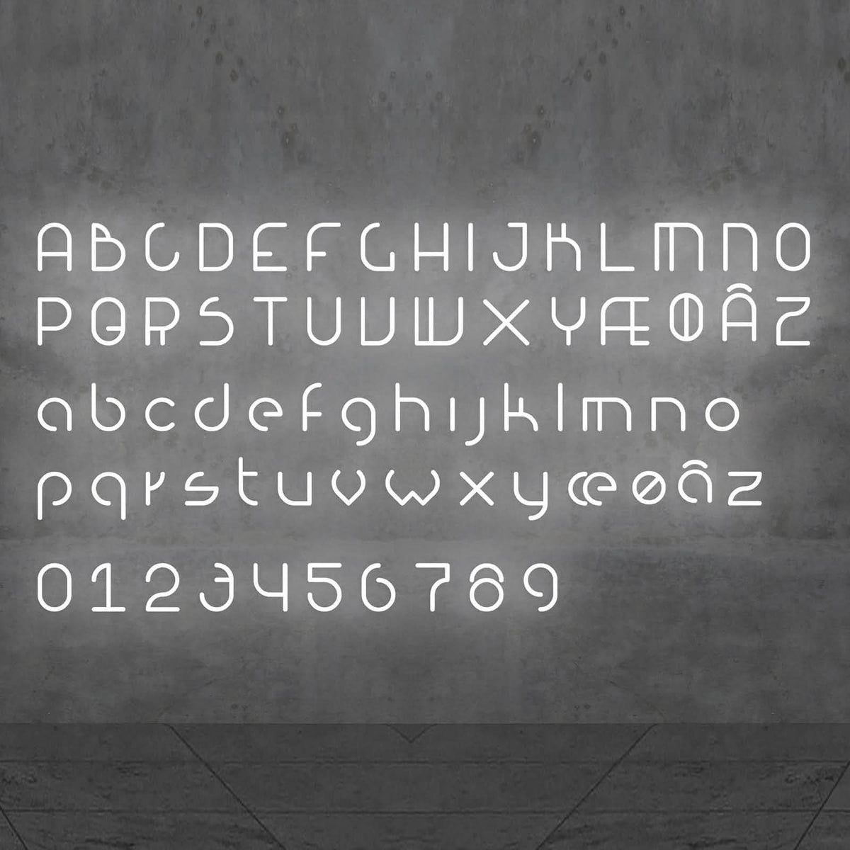 Vue frontale de l’alphabet complet lumineux, majuscules, minuscules et chiffres sur mur gris.