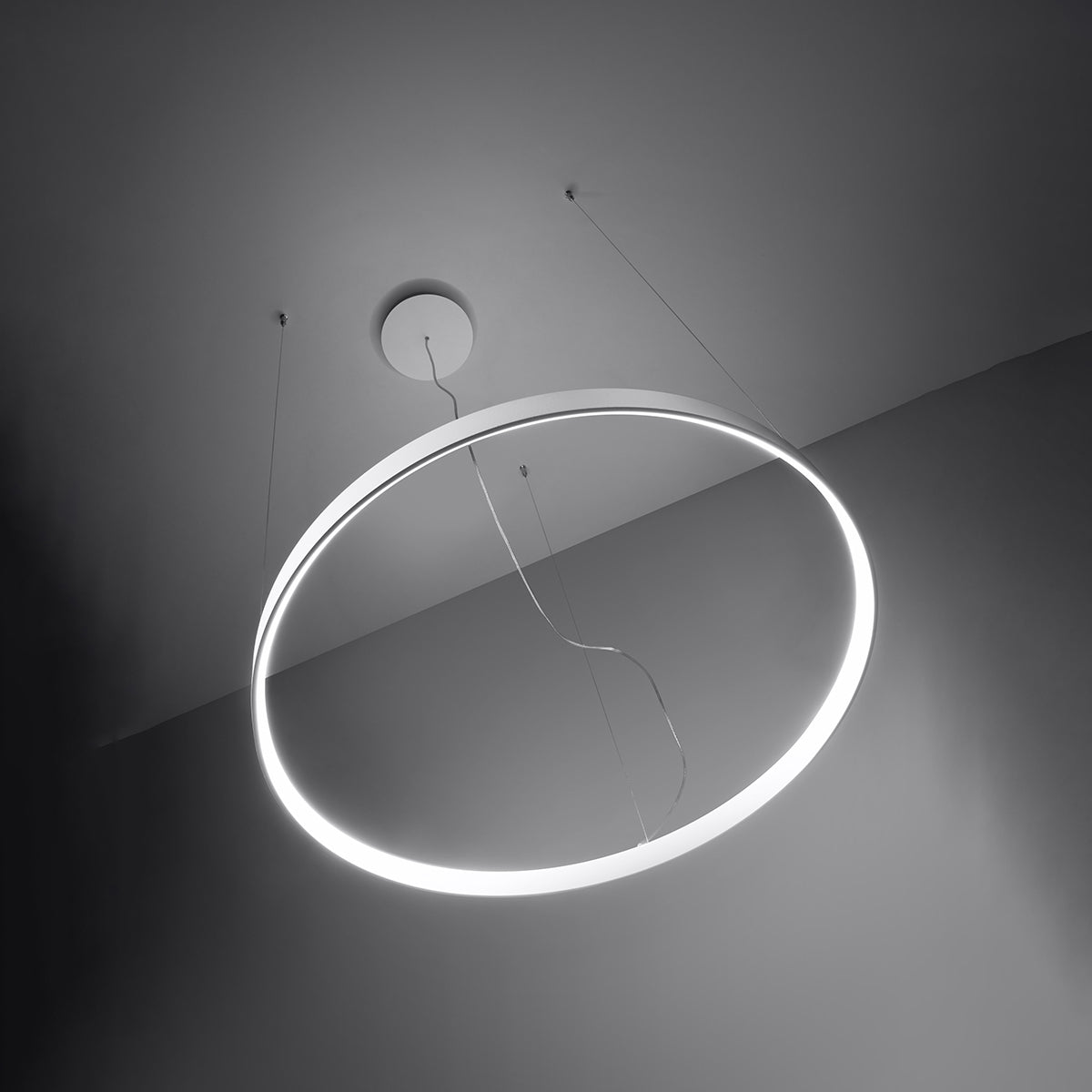 Anneau lumineux suspendu éclairé, halo blanc dans une pièce sombre, vue inclinée.