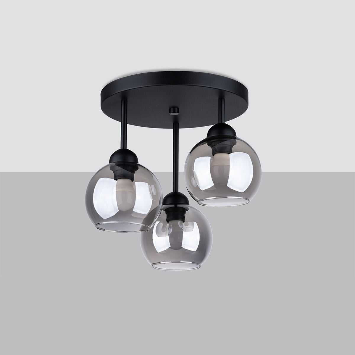 Luminaire noir à trois globes en verre fumé présenté sur fond gris, vue de face.