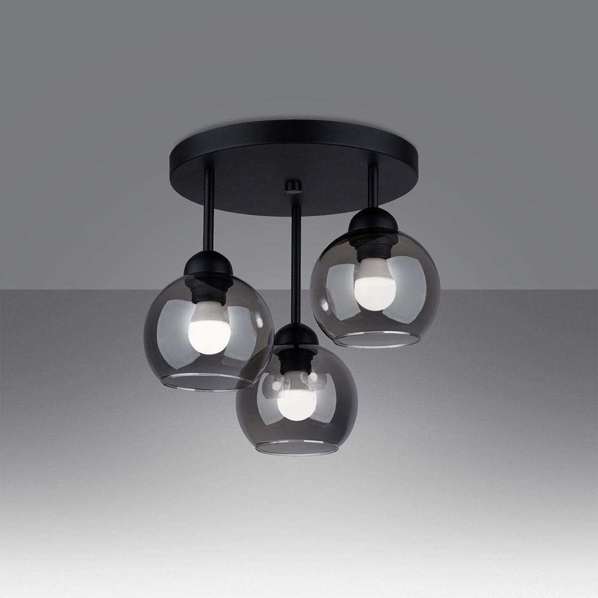 Luminaire allumé sur fond dégradé, ampoules visibles à travers trois globes en verre fumé.