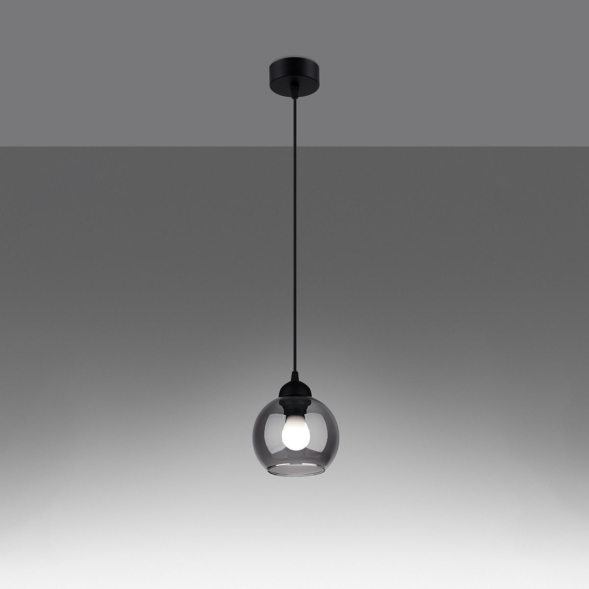 Lampe suspendue allumée, ampoule visible à travers le verre fumé de l'abat-jour.
